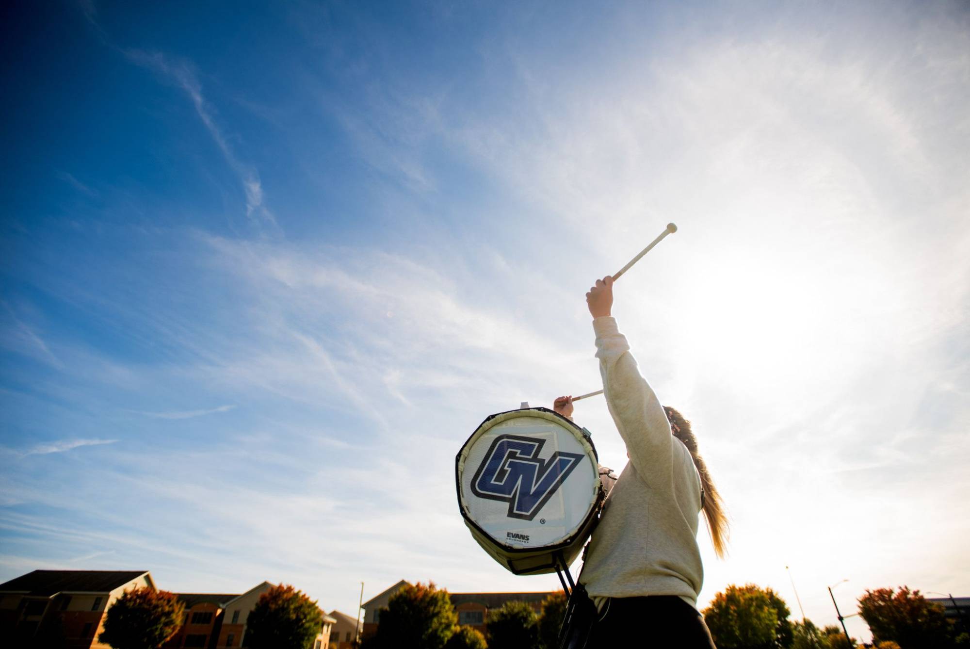 Student is playing a drum with a GV Logo with blue skies above